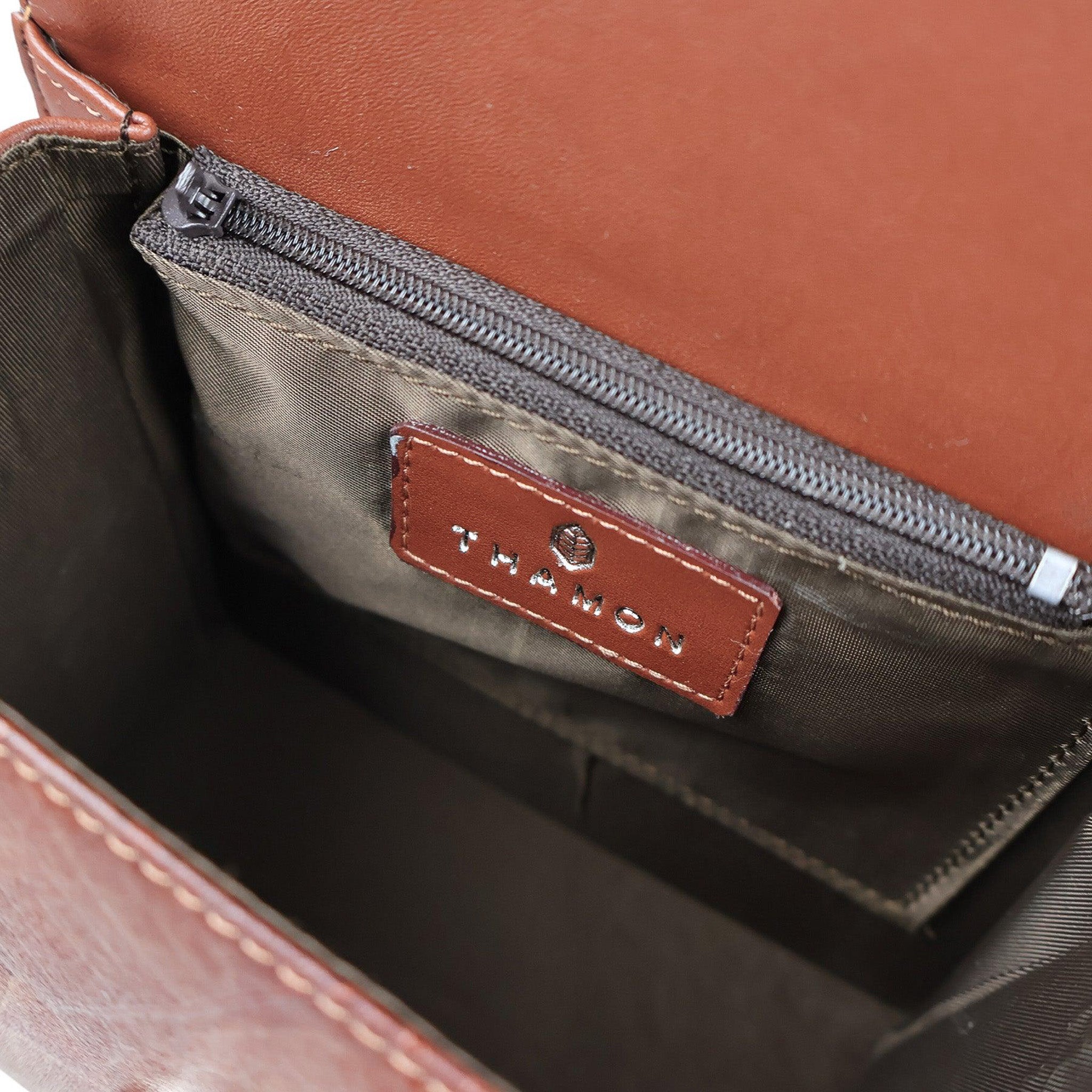 Interior view of the Thamon Spice Brown vegan Leaves Box Bag, featuring a smooth, tawny brown lining with a zippered pocket, and a leather patch embossed with the Thamon logo, highlighting the bag's practical design and luxurious feel