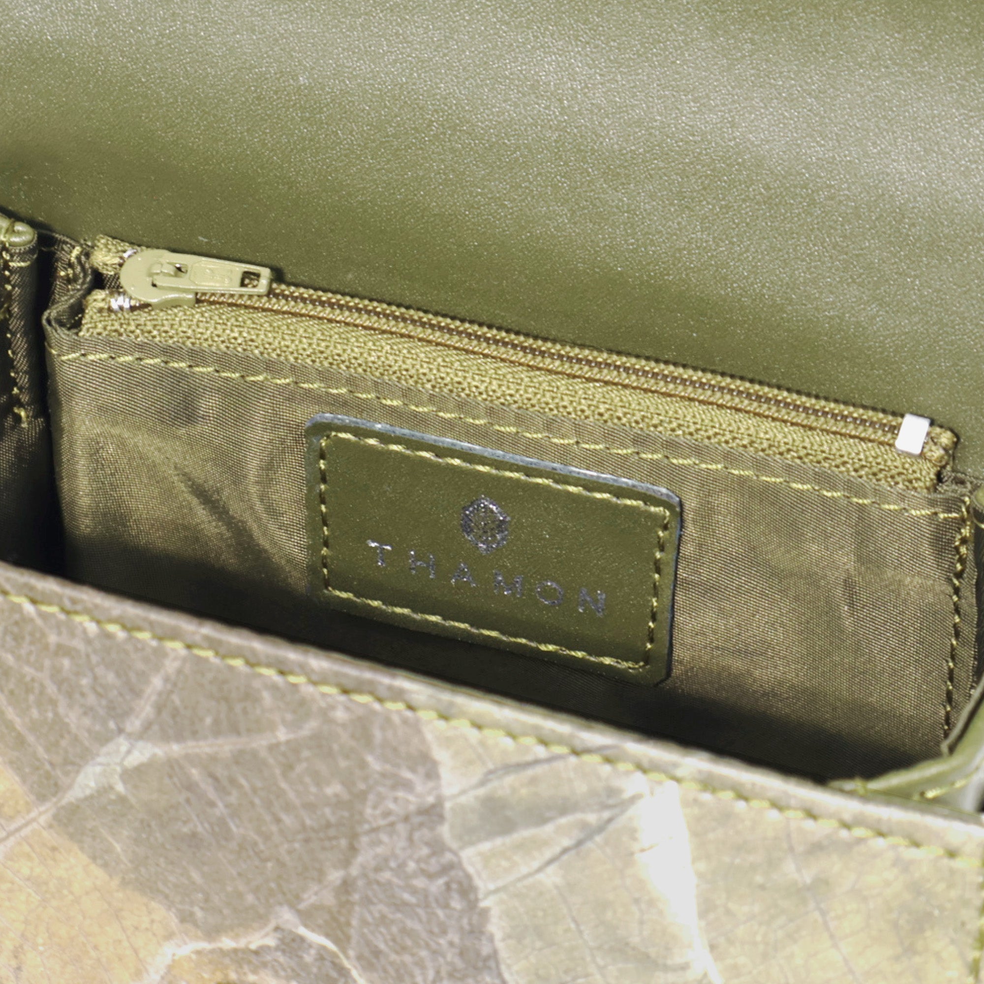 Close-up of the interior of a sustainable Thamon wallet made from Leaftex vegan leaf leather, showing olive green fabric lining, secure zip pocket, and embossed brand logo tag. Eco-friendly, cruelty-free wallet design combining natural leaf texture with durable craftsmanship, ideal for ethical and stylish everyday use.