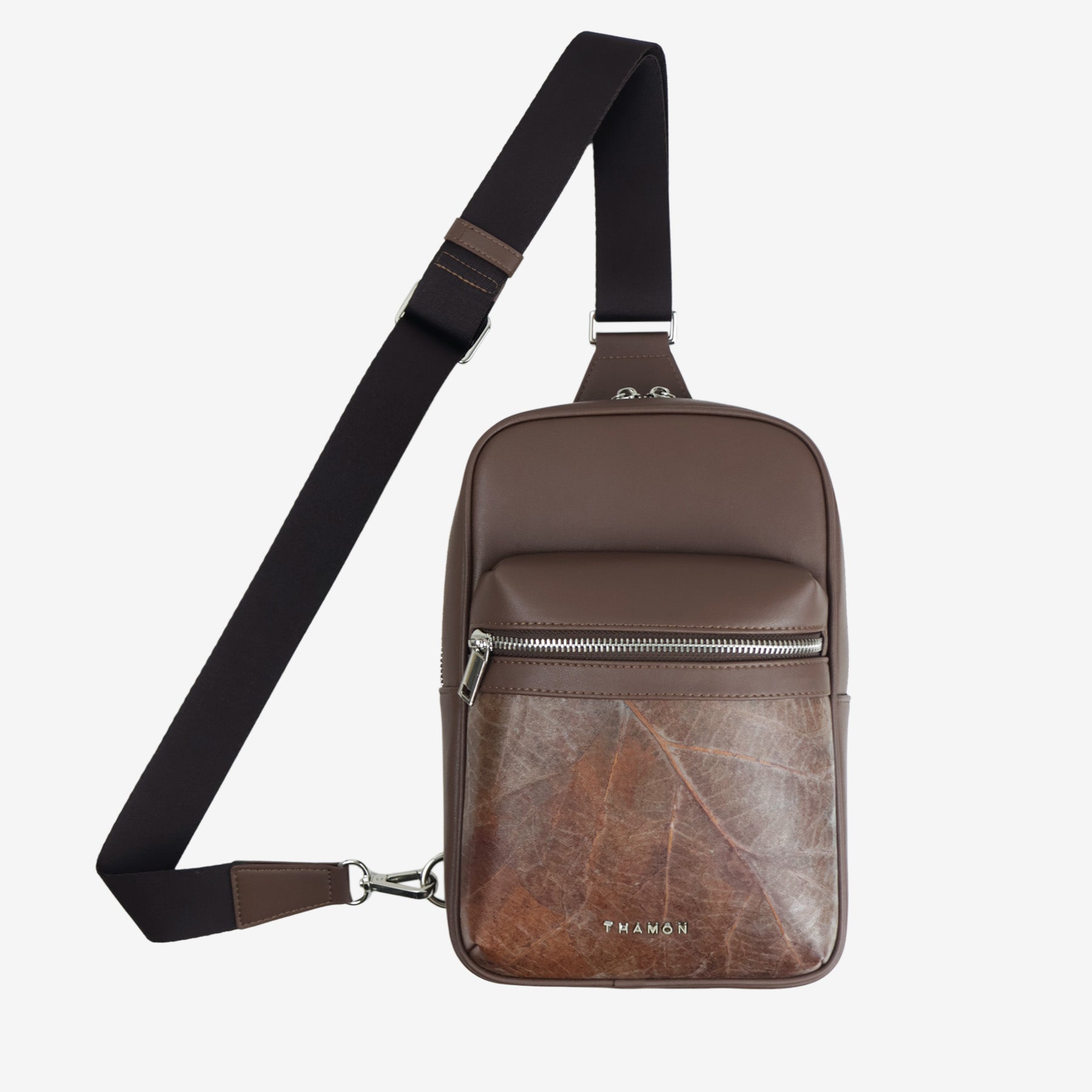 Full front view of Nomad sling bag in walnut brown with adjustable strap, front zip pocket, and natural leaf pattern panel