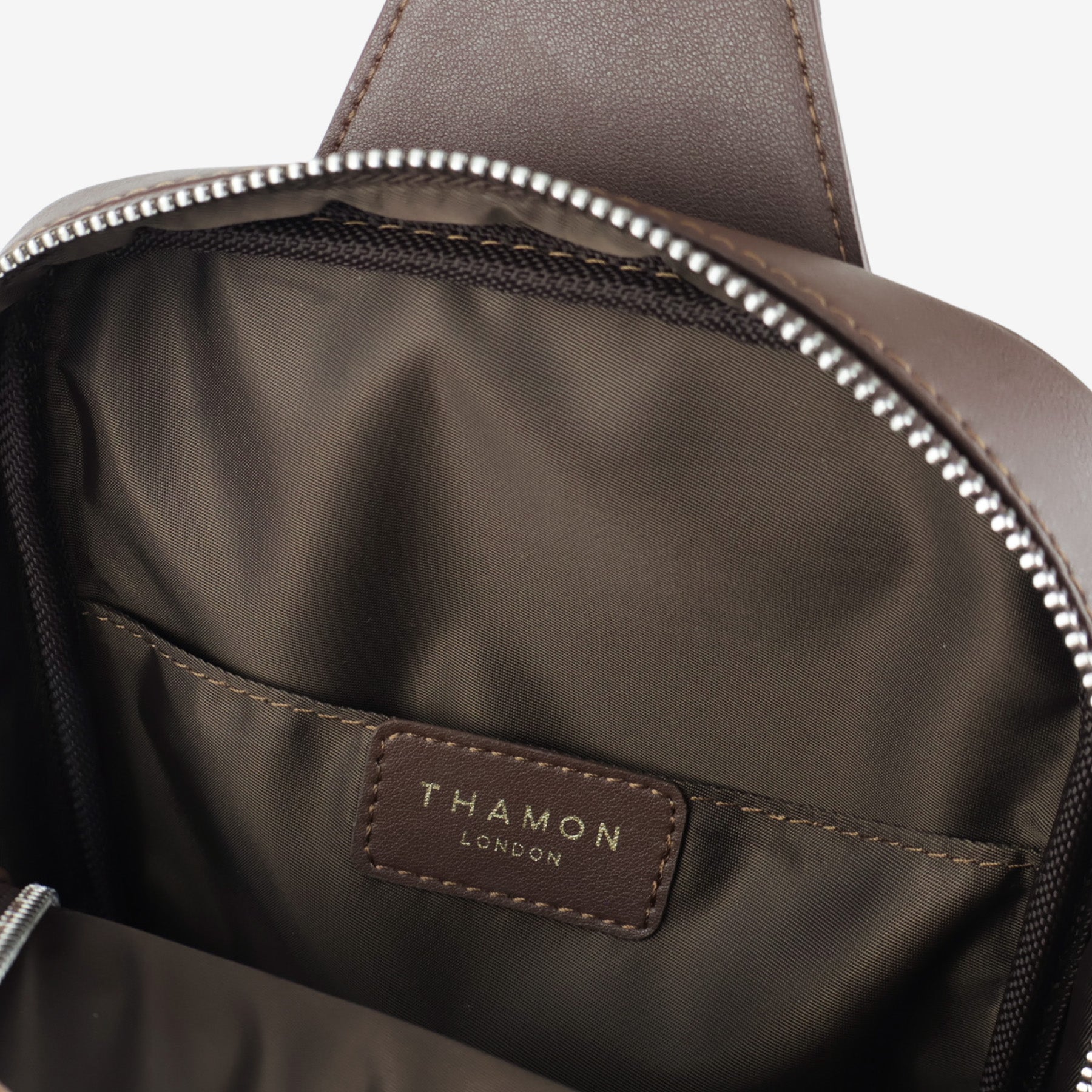 Interior view of Nomad sling bag in walnut brown showing fabric lining, open pocket, and Thamon London logo label