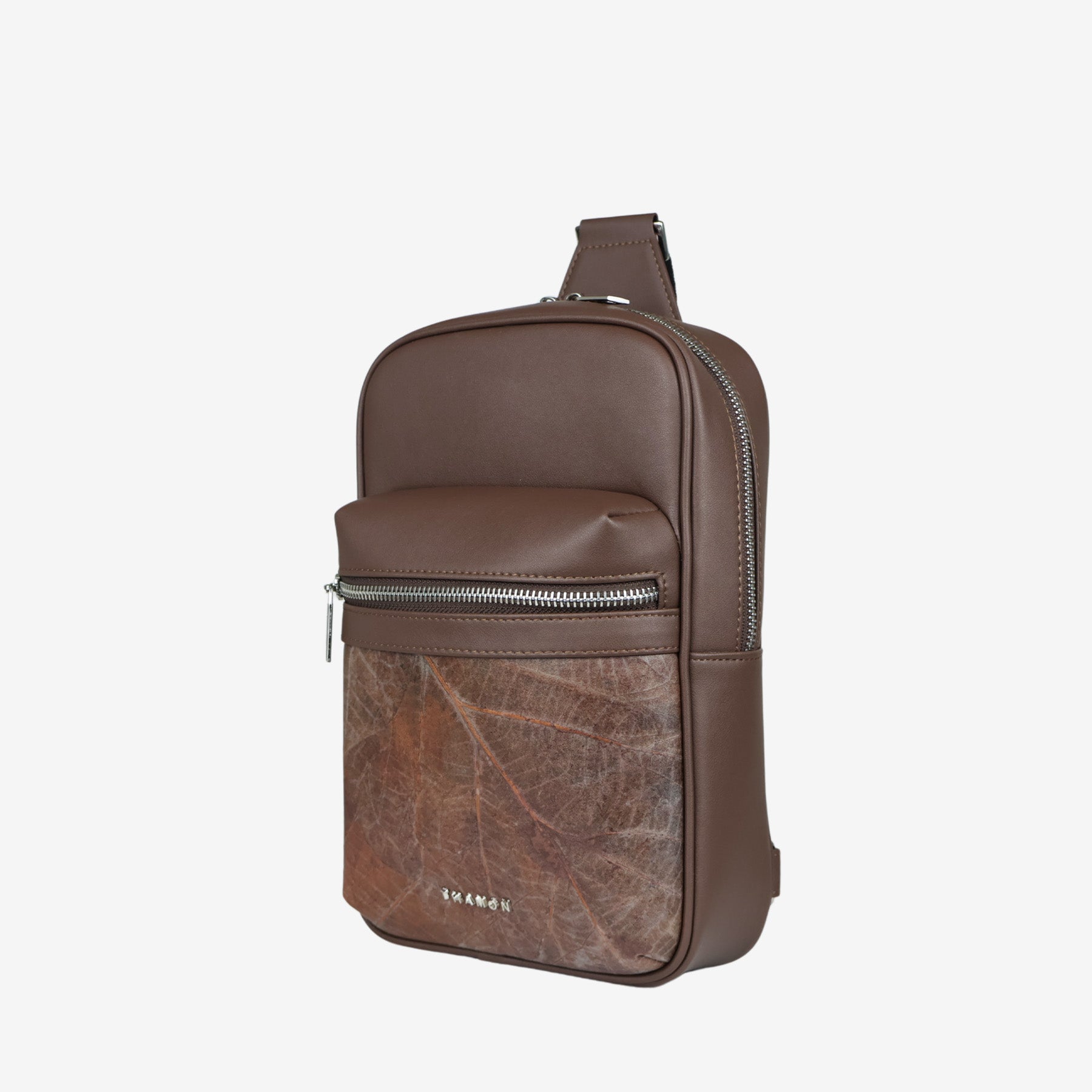 Side view of Nomad sling bag in walnut brown with front zip pocket and natural leaf pattern panel