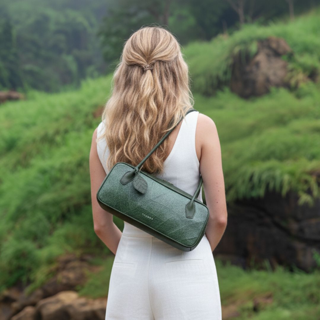 A model in a white outfit carries the Thamon Craugette Shoulder Bag in Forest Green vegan leaf leather, reflecting sustainable elegance in a lush natural setting.
