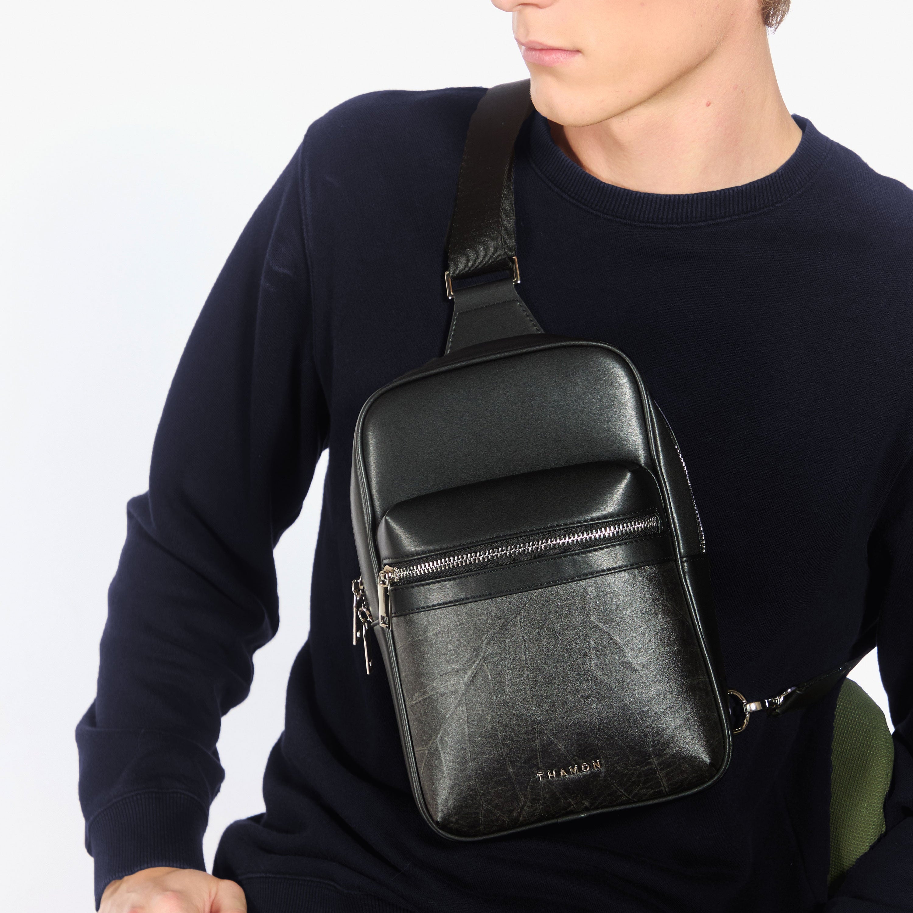 Man wearing black Nomad sling bag made from Leaftex™ (real leaf leather), styled crossbody over navy sweater