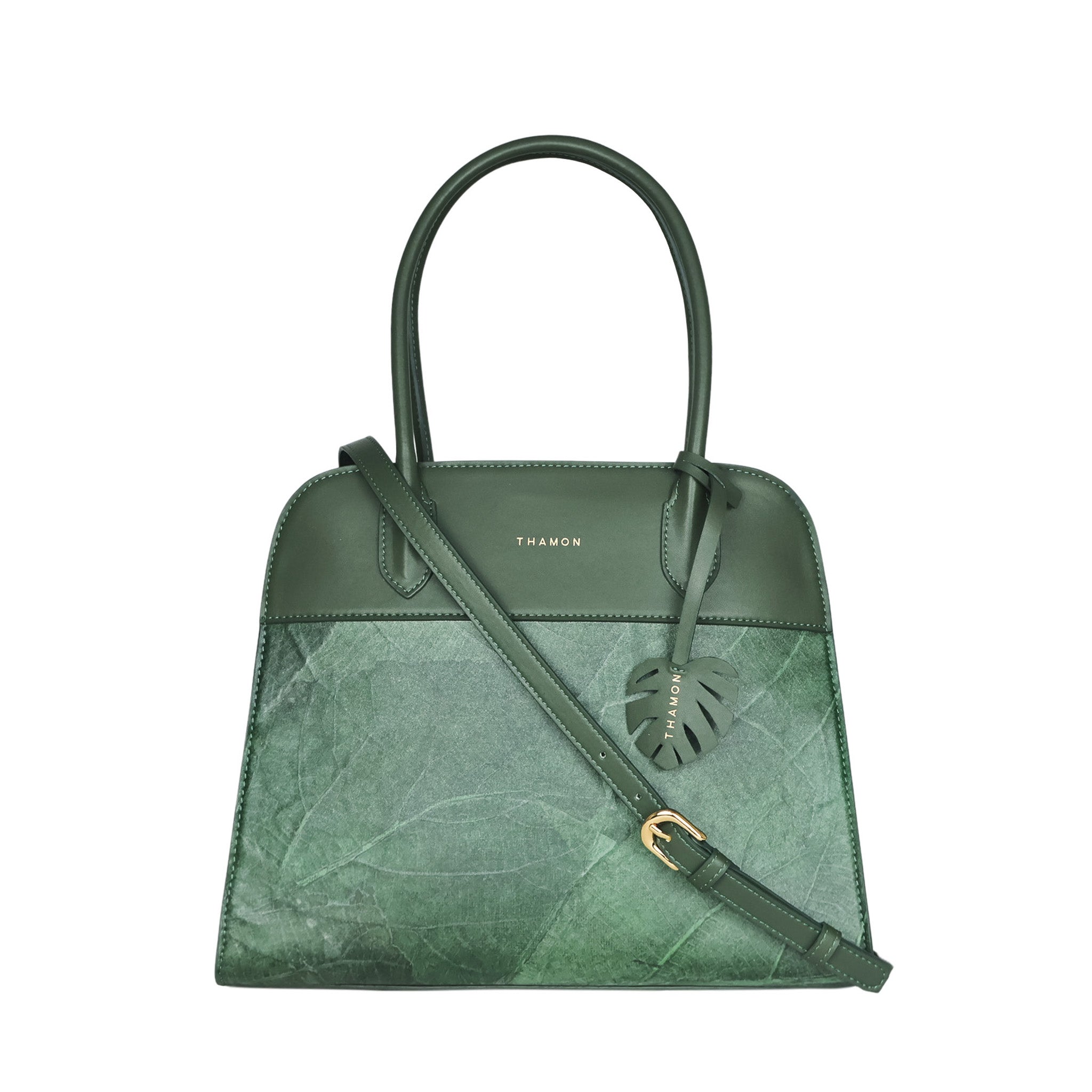 Sloane tote bag in forest green vegan leather with a pressed leaf pattern, featuring an adjustable crossbody strap, sturdy top handles, and a decorative leaf-shaped tag on the front.