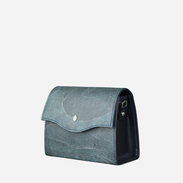 A side view of a blue Dianne box-style vegan crossbody bag by Thamon showcasing the leaf imprint texture and the contrast of the dark blue side panel against a white background.