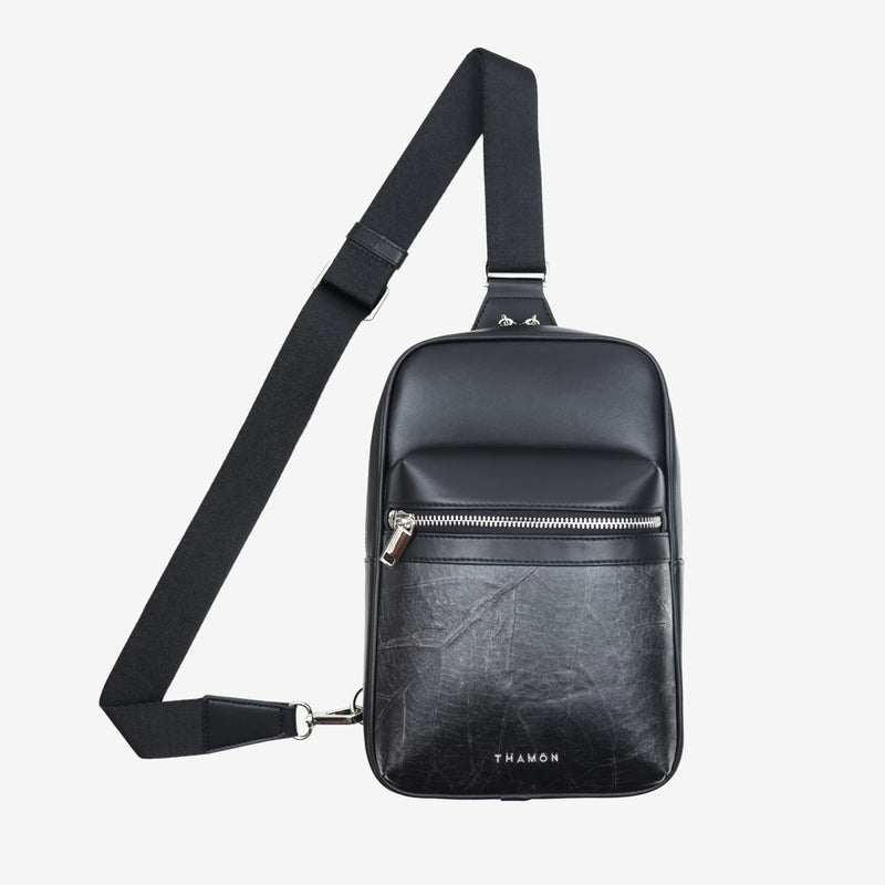 Front with starp view of the Thamon Nomad sling bag in black, featuring a sleek design with a silver-tone zipper, an adjustable strap, and the Thamon logo embossed on the front pocket.