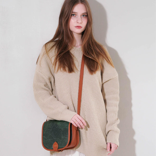 Confident young woman with long brown hair modeling a Thamon Heidi forest green crossbody bag paired with a cozy beige knit sweater, highlighting eco-friendly fashion
