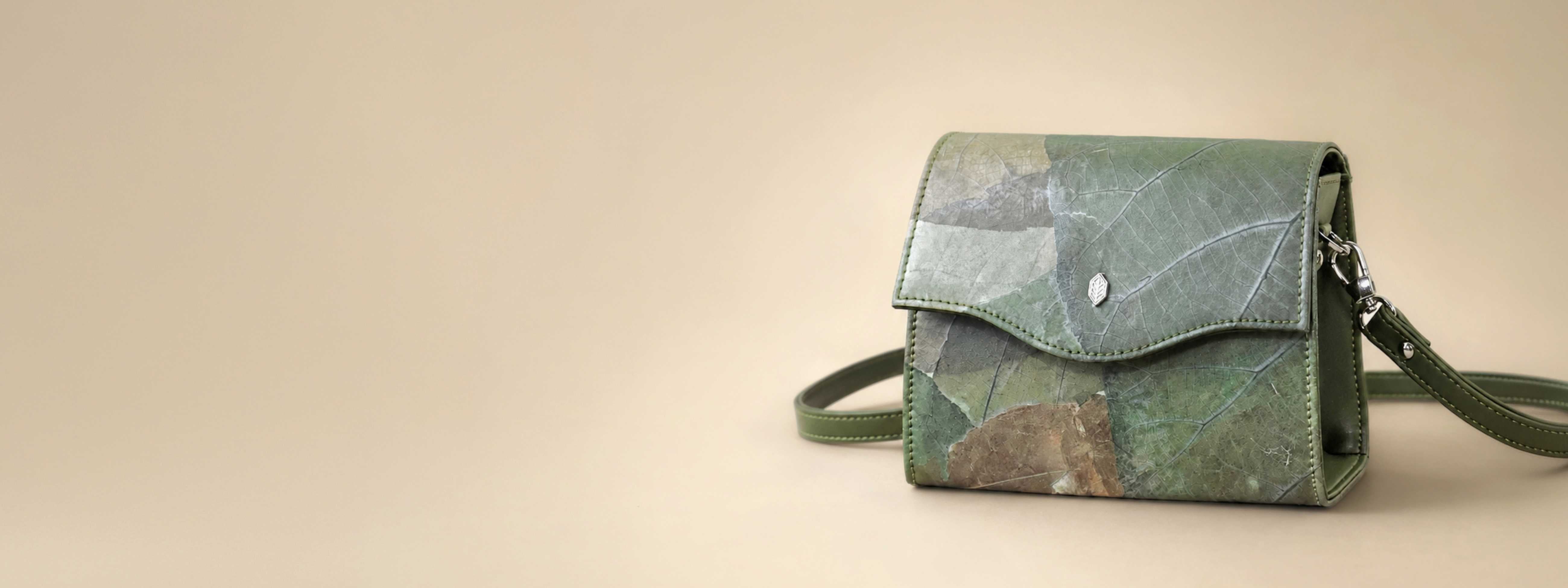 BOX crossbody bag in Moss Green Leaftex on a warm beige background with soft studio lighting.