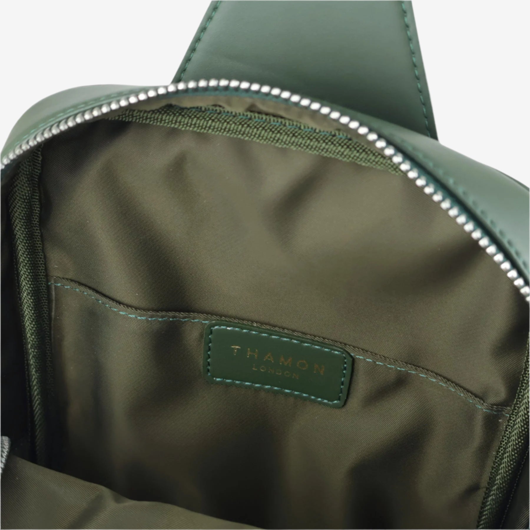 Interior view of forest green Nomad sling bag showing fabric lining, stitched logo label, and internal slip pocket