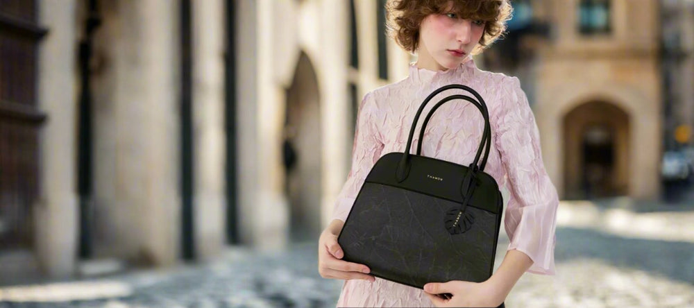 Model in a pink dress holding the Sloane Tote Bag by Thamon, a black handbag with a unique leaf pattern design for sustainable, eco-conscious fashion