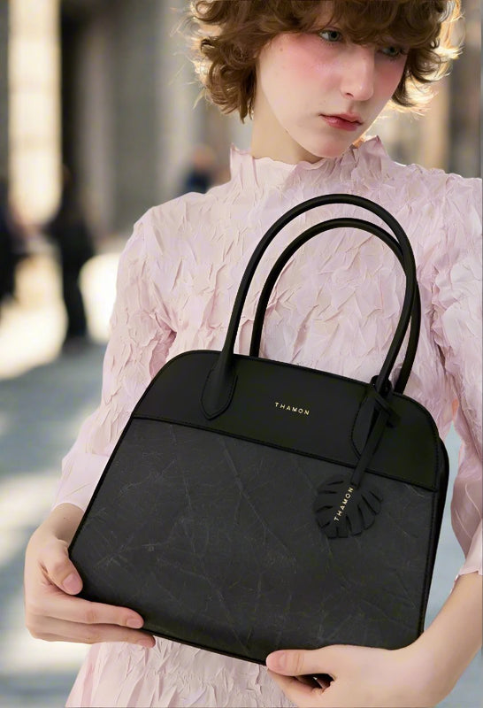 Close-up of model holding the Sloane Tote Bag in black with a leaf pattern, dressed in a pink textured outfit, shown in a mobile-friendly size for outdoor scenes