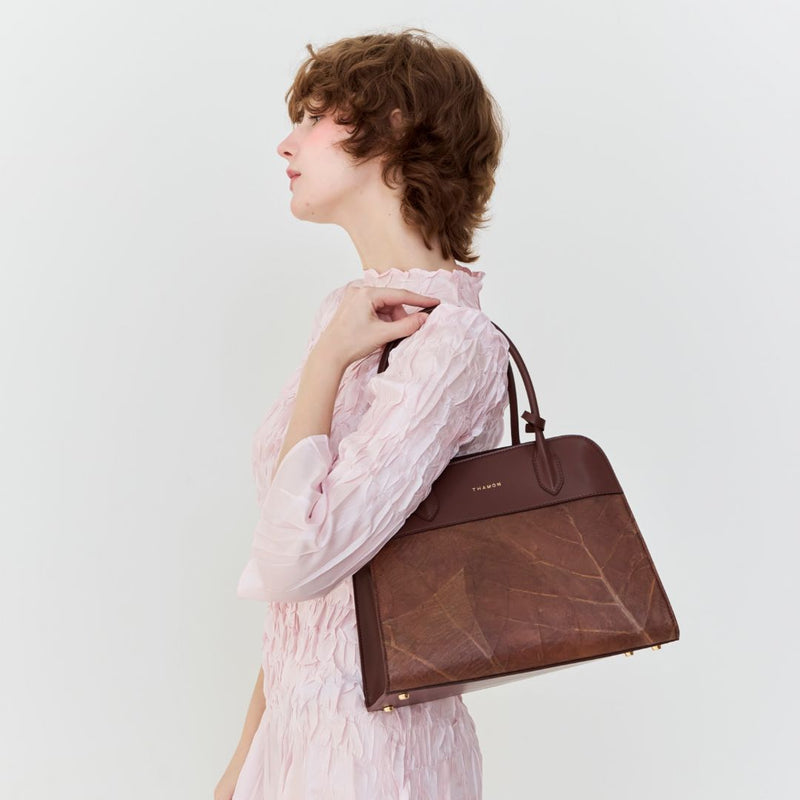 Woman holding the Sloane Tote Bag in spice brown on her shoulder, showcasing the natural leaf pattern and elegant design.