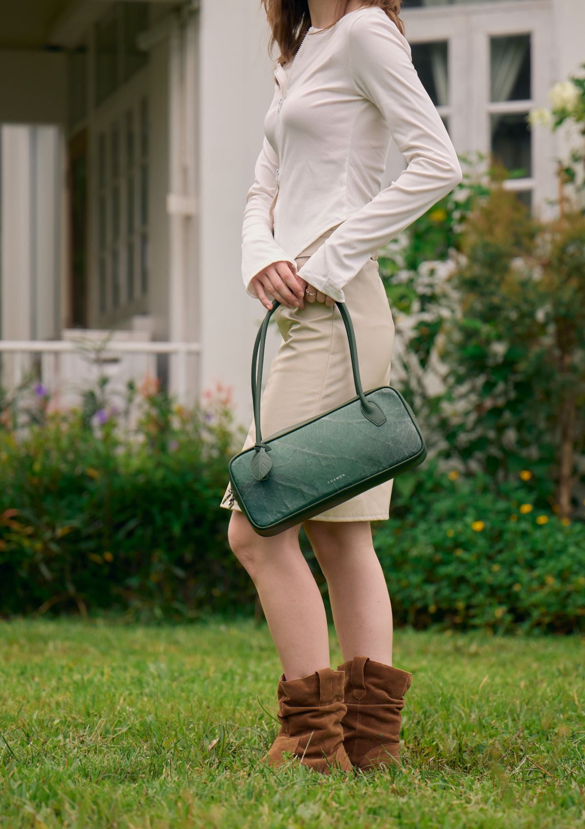 Model carrying the Thamon Craugette Bag in Forest Green Leaftex outdoors with garden background.