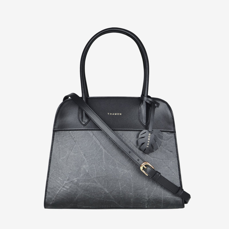 Sloane tote bag in black vegan leather with a pressed leaf pattern, featuring an adjustable crossbody strap, sturdy top handles, and a decorative leaf-shaped tag on the front.