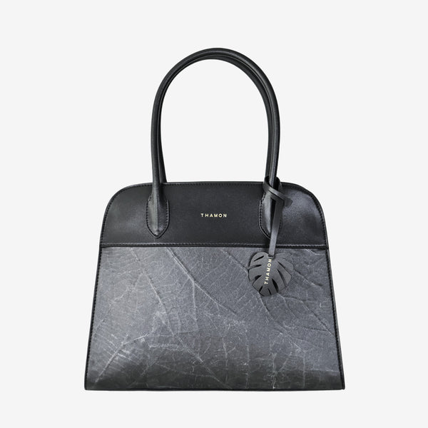 Sloane tote bag in black vegan leather with a pressed leaf pattern, featuring sturdy top handles and a decorative leaf-shaped tag on the front, offering a structured and minimalist design.