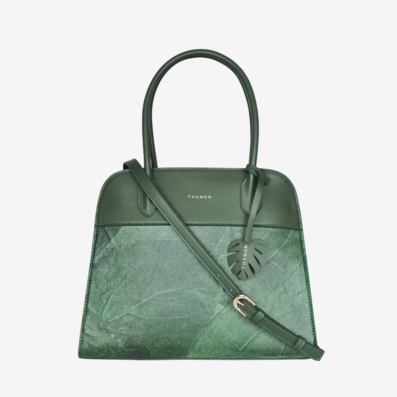 Sloane tote bag in forest green vegan leather with a pressed leaf pattern, featuring an adjustable crossbody strap, sturdy top handles, and a decorative leaf-shaped tag on the front.