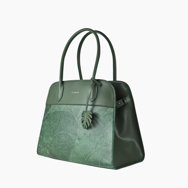 Sloane tote bag in forest green vegan leather with a pressed leaf pattern, side view showing top handles and leaf-shaped tag, featuring a structured silhouette and smooth sides.