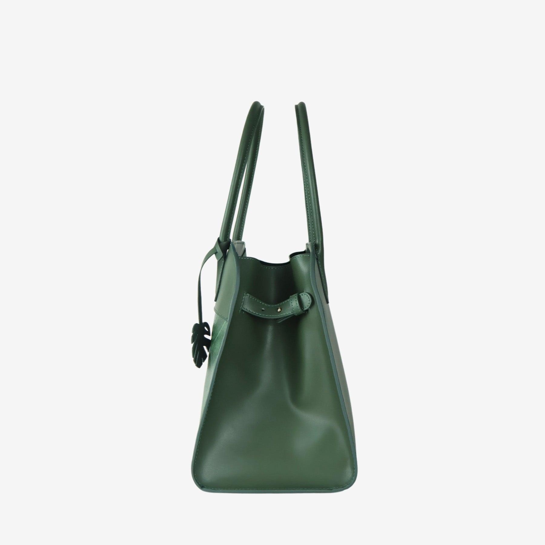 Side profile of the Sloane tote bag in forest green vegan leather, showing a smooth, structured surface and sturdy top handles. The bag's leaf-shaped tag is visible near the front, with a minimal and sleek design.