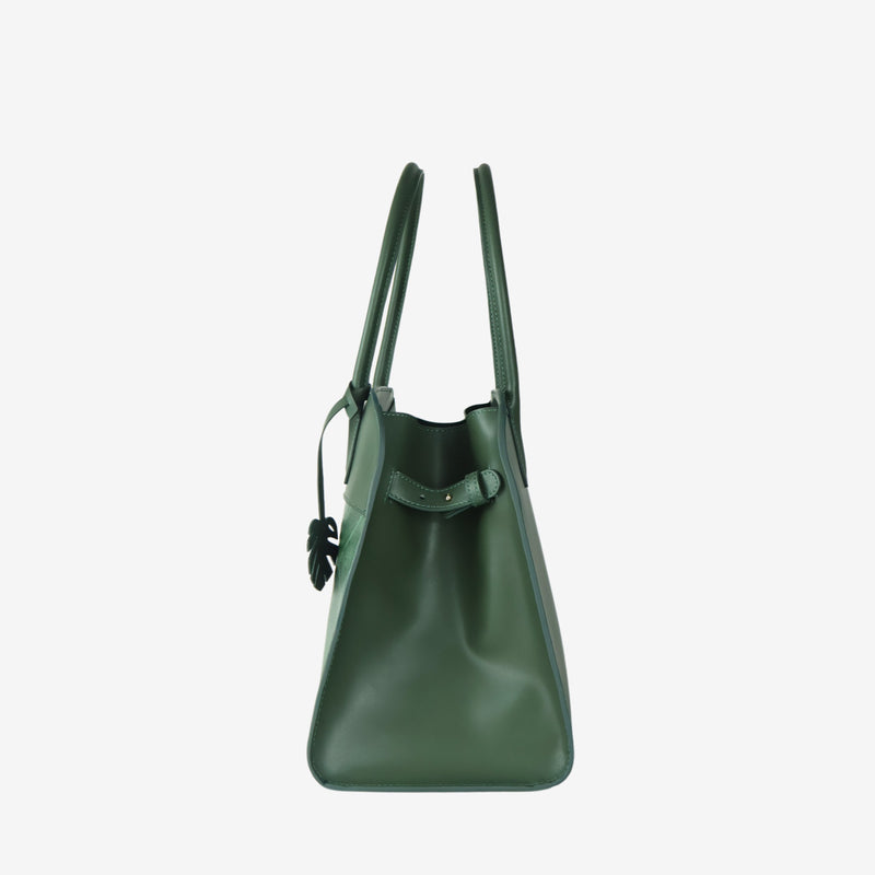 Side profile of the Sloane tote bag in forest green vegan leather, showing a smooth, structured surface and sturdy top handles. The bag's leaf-shaped tag is visible near the front, with a minimal and sleek design.