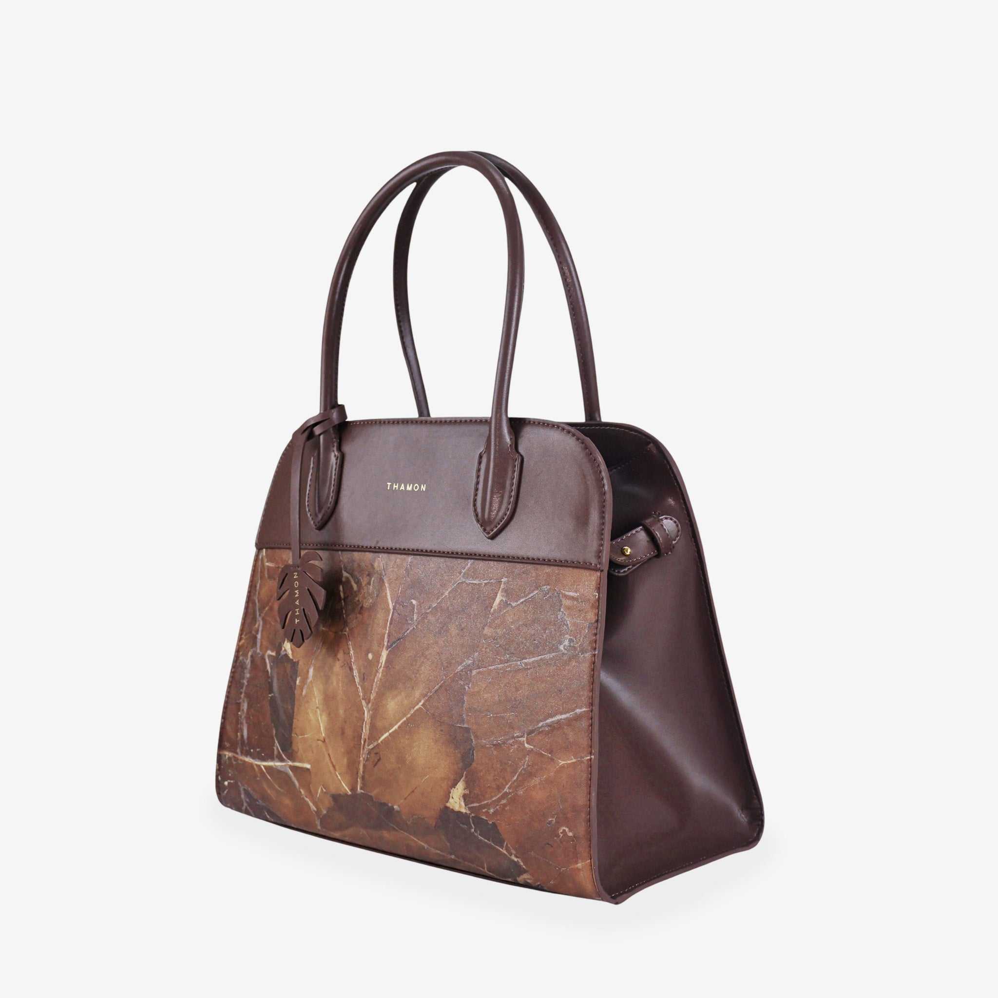 Side view of the Sloane tote bag in spice brown vegan leather with a pressed leaf pattern, featuring sturdy top handles, a structured silhouette, and a decorative leaf-shaped tag attached to the front handle.
