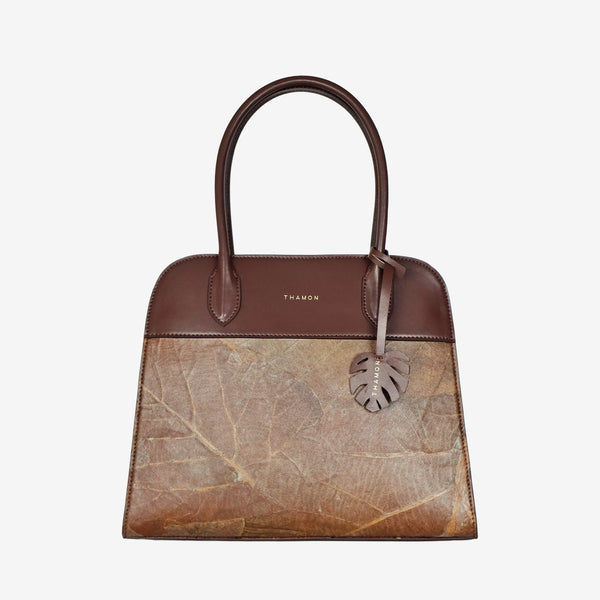 Sloane tote bag in spice brown vegan leather with a pressed leaf pattern, featuring sturdy top handles and a decorative leaf-shaped tag on the front, showcasing a natural and earthy design.