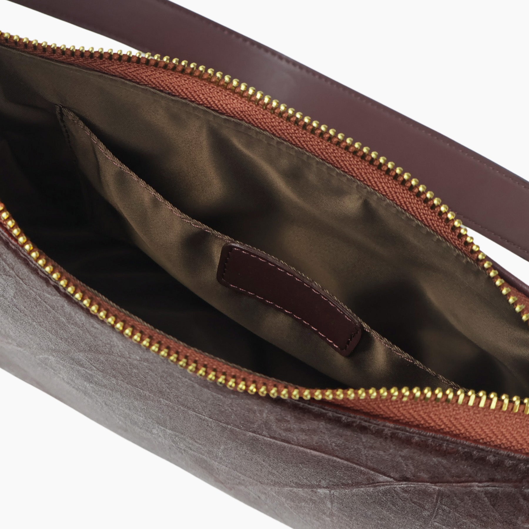 Close-up of an open walnut brown textured leaf leather maki handbag showing a dark brown satin-lined interior with a gold-tone zipper and a small brown veagn leather Thamon brand tab.