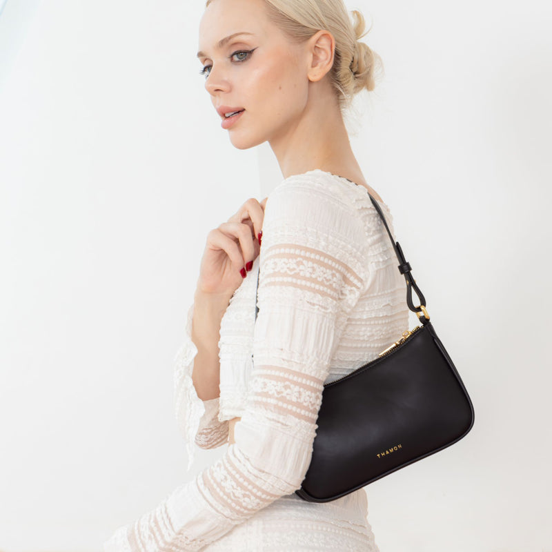 A woman wearing a white blouse and white pants, carrying the Mila Black Vegan Shoulder Bag with a vegan leather side