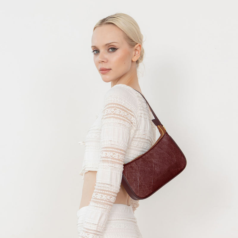A woman wearing a white blouse and white pants, showcasing the Mila Spice Brown Vegan Shoulder Bag with a detailed leaf pattern
