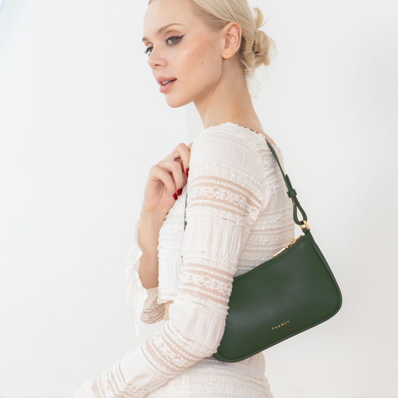 A woman wearing a white blouse and white pants, carrying the Mila Forest Green Vegan Shoulder Bag with a vegan leather side