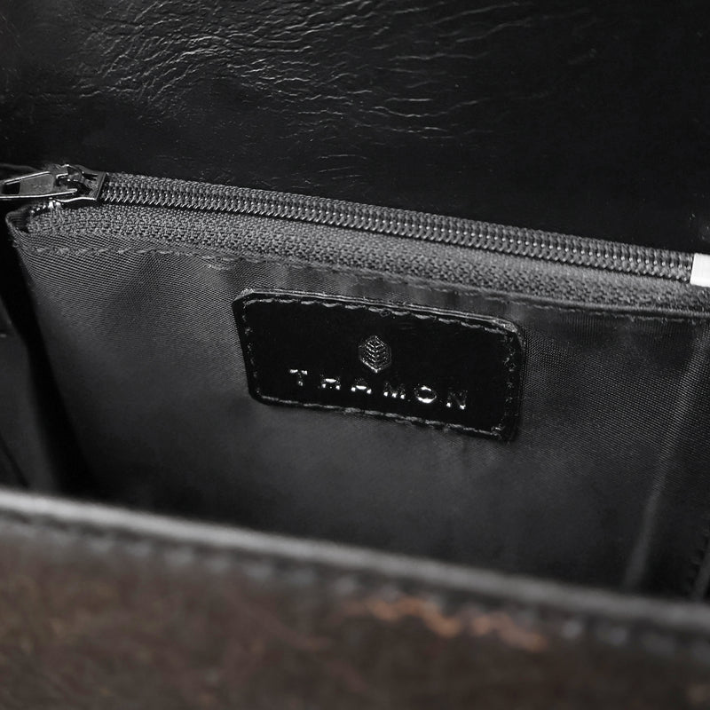 Interior detail of Thamon London's black leaf leather box bag featuring the brand's logo embossed on a black vegan leather patch above the zippered pocket, accentuating the bag's high-quality craftsmanship.