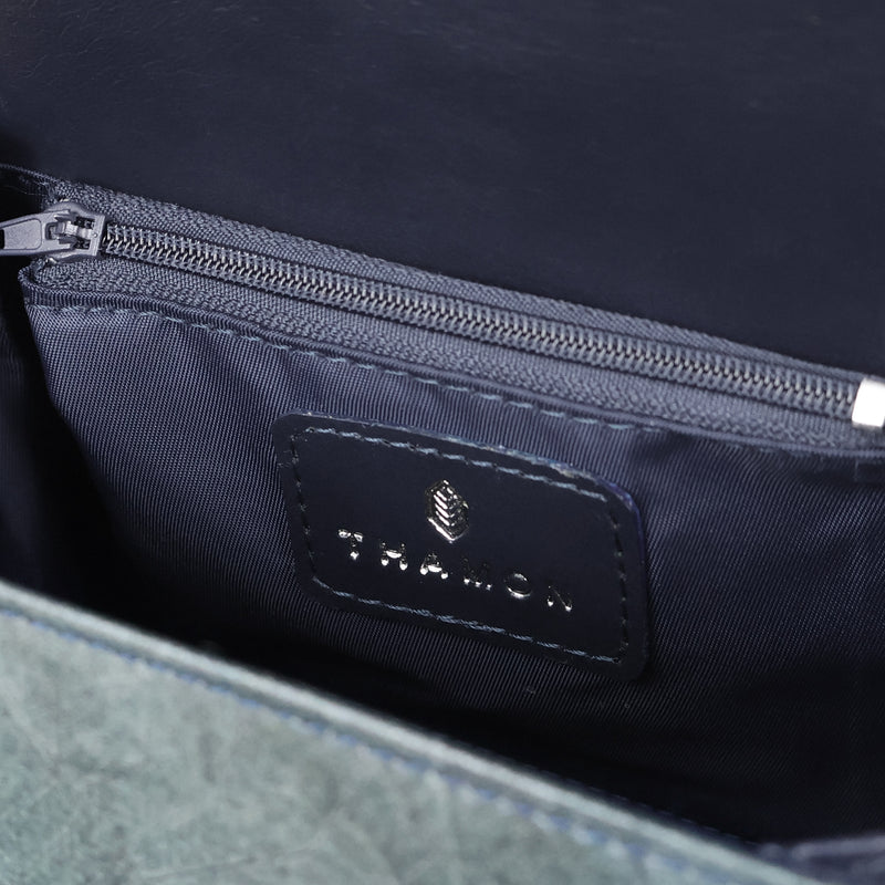Close-up view of a luxurious dark interior of a Thamon branded vegan crossbody bag, featuring a detailed black label with the Thamon logo in silver and a matching zipper compartment, highlighting the brand's elegant design against the blue textured material.