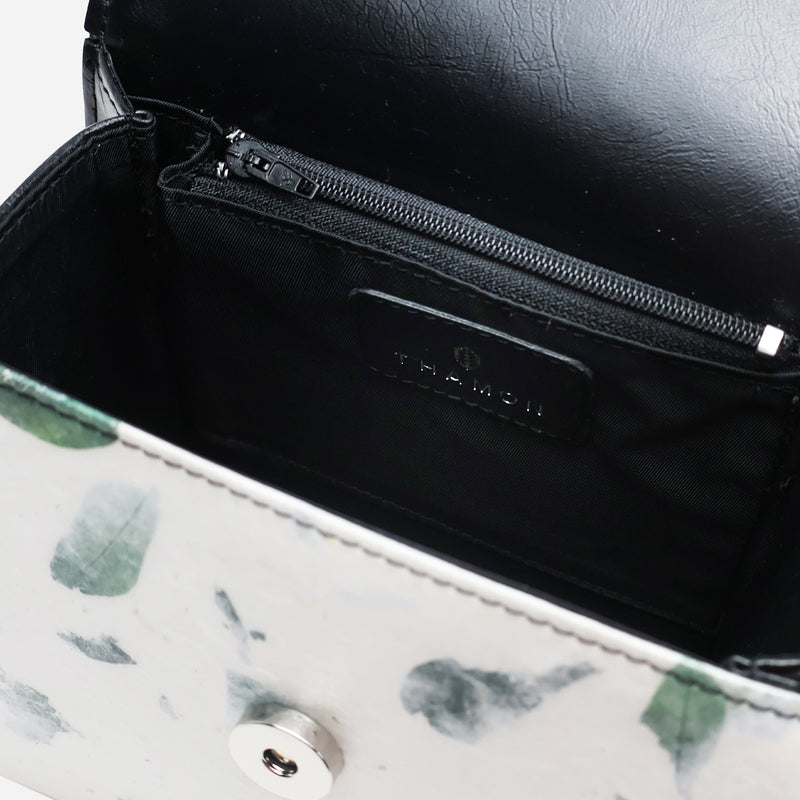 Interior view of the Thamon camouflage leaf box bag, highlighting the sleek black lining, an embossed logo on a vegan leather patch, and a zippered pocket for secure item storage.
