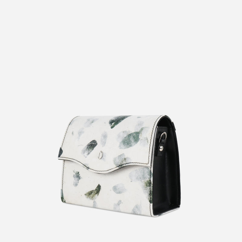 Side view of the Thamon camouflage leaf box bag, featuring a white base with a green leafy pattern, a curved flap, and a glossy black side panel, with a visible metal loop for the strap attachment.