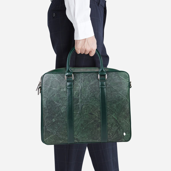 A man in a white shirt and navy trousers holding a forest green leaf leather Cambridge briefcase by Thamon.