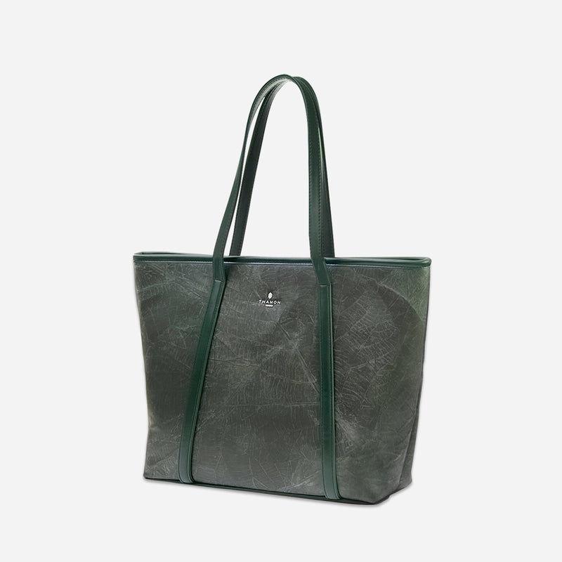 Side angle view of the Thamon forest green Alma tote bag, displaying the rich leaf leather texture, reinforced edges, and long shoulder straps, with a silver-plated Thamon logo on the front, against a minimalistic background