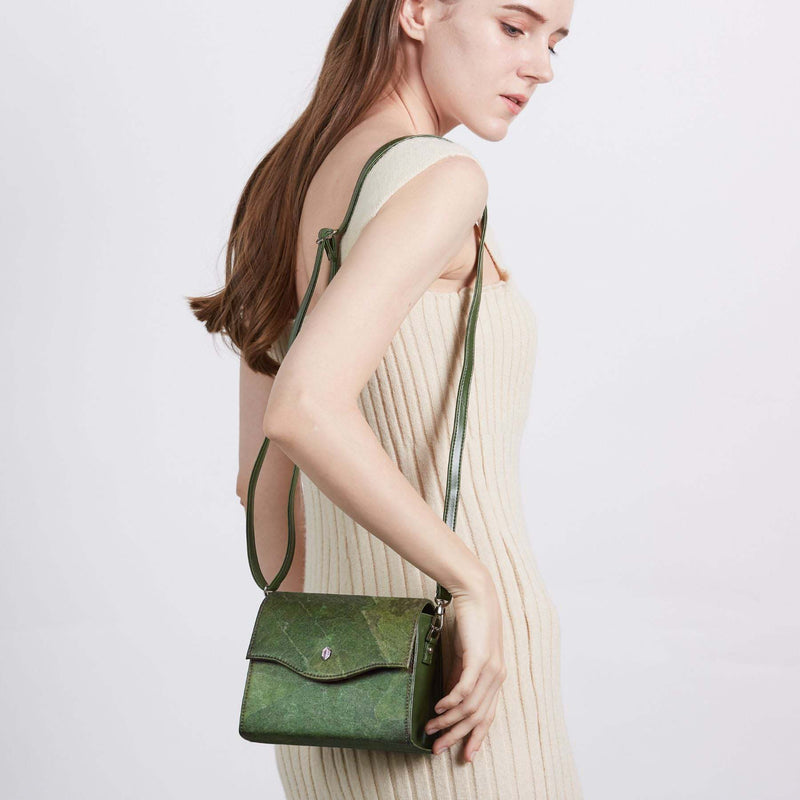 A woman in a cream knit dress wears the Thamon Forest Green Leaf Leather Box Bag as a crossbody, the bag's natural green leaf textures visible against the soft fabric of her dress, blending fashion with sustainability.